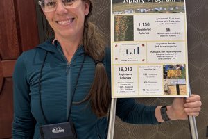 Photo of Brooke Decker, who has been elected President of the Apiary Instructors of America. She is smiling at the camera while holding a sign that details an Apiary Program.