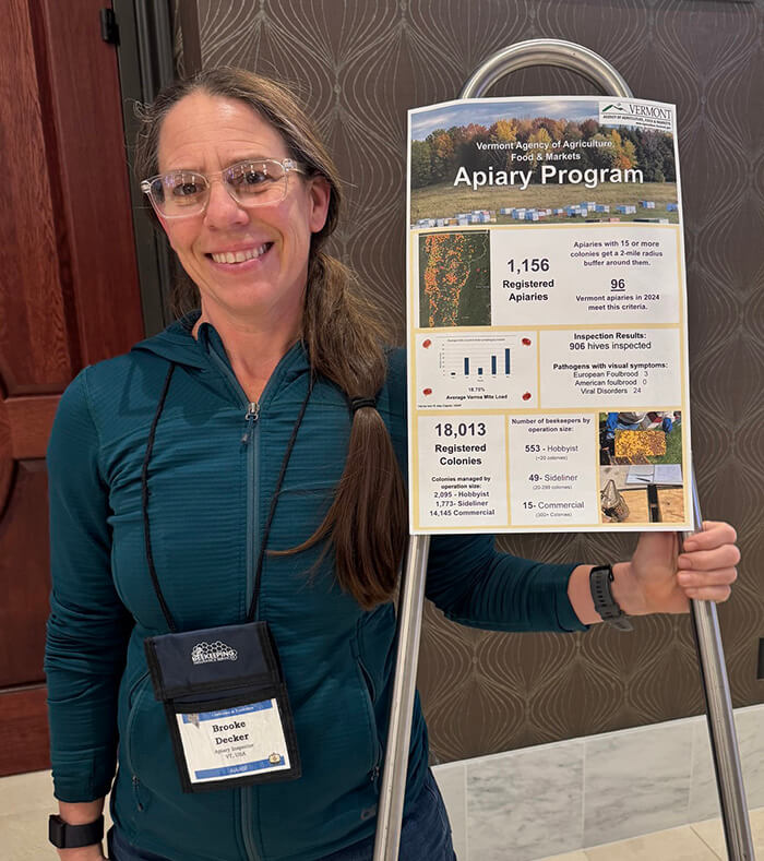 Photo of Brooke Decker, who has been elected President of the Apiary Instructors of America. She is smiling at the camera while holding a sign that details an Apiary Program.